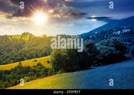 countryside mountain landscape of ukraine. day meet night. sun and moon over rural fields and forested hills at twilight. remote place of mizhhirya di Stock Photo