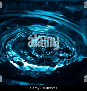 403.A dark, detailed close-up of a water droplet creating a splash and ripples on a dark liquid surface, showcasing the chaotic and dynamic texture in Stock Photo