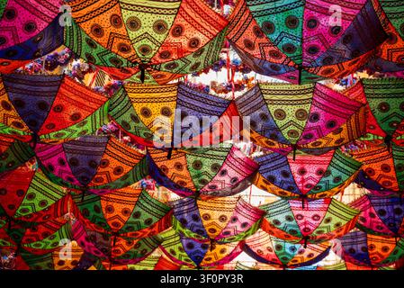 Vibrant canopy of colorful, patterned umbrellas hanging overhead as a festive street decoration, creating a beautiful mosaic of light Stock Photo