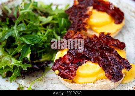 Delicious eggs benedict on toasted English muffins topped with crispy bacon and creamy hollandaise sauce, served with a side salad Stock Photo