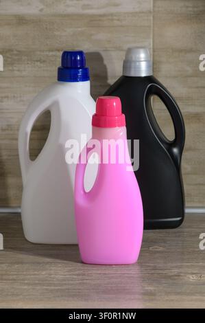 A professional product photograph featuring three plastic detergent bottles in vibrant pink, white, and matte black, arranged on a wooden surface agai Stock Photo