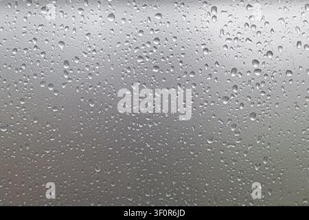 Raindrops on frosted glass window. Raindrops bead across a frosted glass window, forming a soft gray abstract texture with blurred outdoor shapes Stock Photo