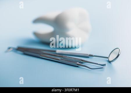 Close-up of stainless steel dental instruments with a white tooth model on a soft blue background, representing dentistry, oral hygiene, dental checku Stock Photo