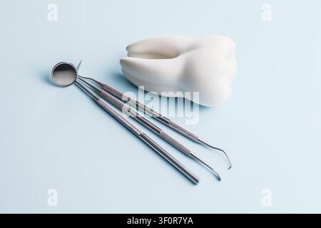 Close-up of stainless steel dental instruments with a white tooth model on a soft blue background, representing dentistry, oral hygiene, dental checku Stock Photo