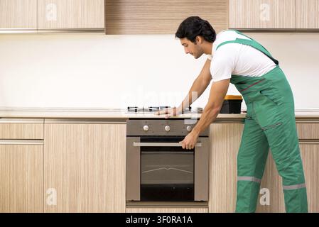 Young contractor repairing oven in kitchen Stock Photo