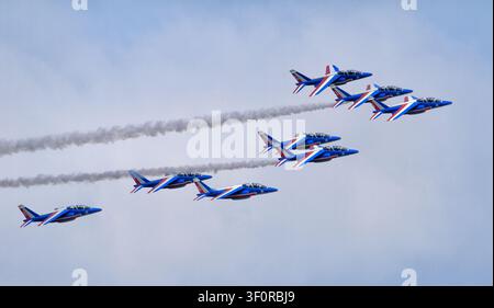 Patrouille de France fly a seven‑ship formation through a cloudy sky, two jets trailing white smoke in a precise aerobatic display. Stock Photo