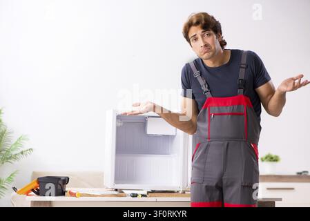 Young handsome contractor repairing fridge Stock Photo