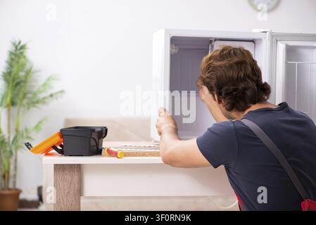 Young handsome contractor repairing fridge Stock Photo