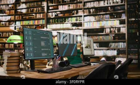 Multiple computer monitors show virtual assistant and blue display on interfaces at library study desk. Space with stacked books, green lamps and keyboards in computer lab. Stock Photo