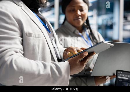 Data center software developer uses a tablet to update server software, supporting reliable infrastructure operations. Stock Photo