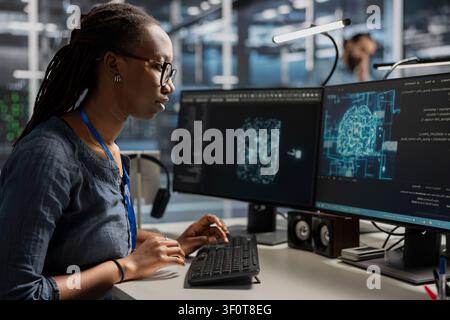 Server facility engineer applying AI ML tech. African American woman in server environment working with AI programming tools on workstation to update equipment. Stock Photo
