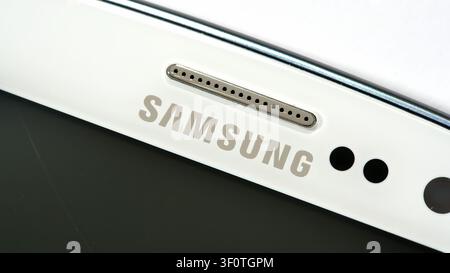 Samsung smartphone logo and earpiece speaker macro, closeup of white older mobile phone top bezel with front sensors and camera holes, electronics rep Stock Photo