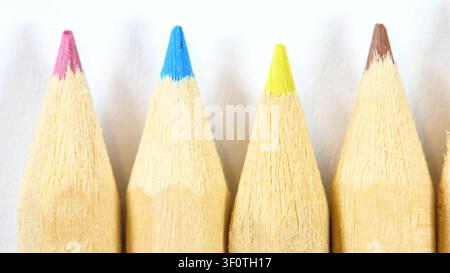 Colored pencil tips in a neat row, extreme macro of sharpened crayons with pink, blue, yellow and brown points on pale paper, school art supplies, cre Stock Photo