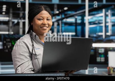 Cheerful server facility software engineer applying AI neural network models. Cheerful server environment staff member works with AI programming tools on workstation, setting up specialized hardware. Stock Photo