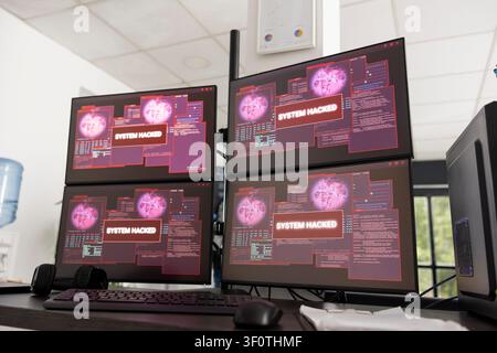 Desktop monitors in vacant office display warning messages indicating unauthorized access to company system. Empty workstations show hacked system alerts and compromised network security. Stock Photo