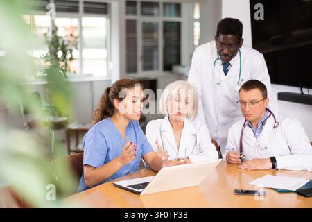 Doctors sitting around the table looking at the notebook Stock Photo