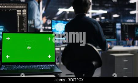 Software developer uses a green screen laptop to manage AI systems, machine learning workflows and server performance. Stock Photo