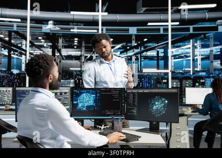 Server room manager supervising work done by engineer working with deep learning models to review data sets. Stock Photo