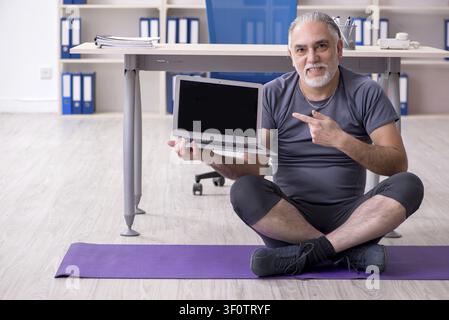White bearded old man employee doing exercises in the office Stock Photo