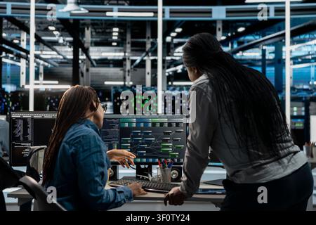 Data center supervisor supervising technical work from systems engineer applying AI to reduce downtime. Stock Photo