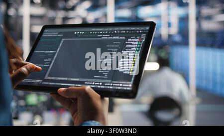 Data center programmer uses a tablet to update server software, supporting reliable infrastructure operations. Stock Photo