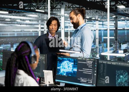 Programmers collaborating, coding in server room, updating deep learning scripts. Stock Photo