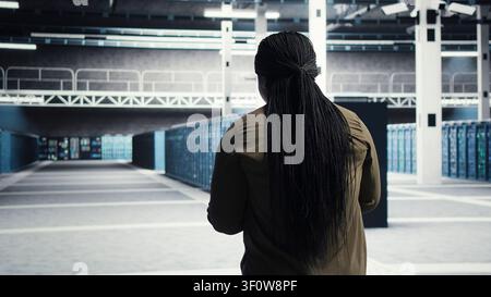Woman walking through server facility rows of servers, rolling out advanced cooling and power management solutions. IT expert supervising server environment, reducing energy consumption. Stock Photo