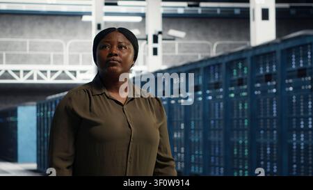 IT administrator walking through server facility rows of servers, rolling out advanced cooling and power management solutions. IT specialist supervising server facility, reducing energy consumption. Stock Photo