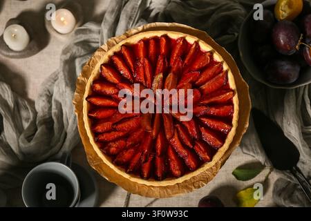 Wooden stand with tasty plum pie, cups and spatula on table Stock Photo