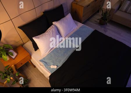 Electric heating pad on big bed in dark room, top view Stock Photo