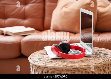 Red headphones on a laptop keyboard with a brown leather sofa and book in the background, home entertainment and relaxation Stock Photo