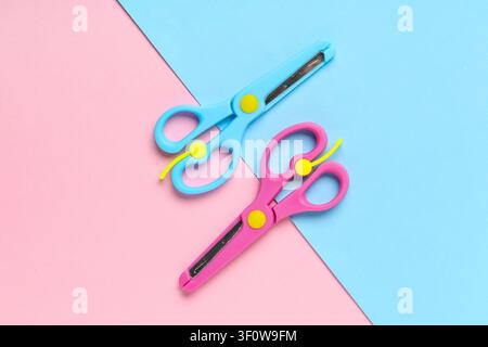 Pink and blue childrens safety scissors with yellow accents on a split pastel background, top view, the scissors feature yellow accents on their pivot Stock Photo