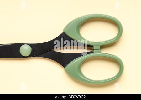 Green handled scissors with black blades office and school supplies craft and cutting tools isolated on a light yellow background Stock Photo