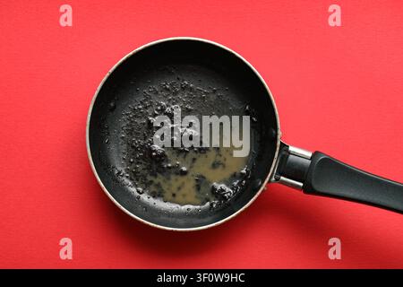 Dirty frying pan with leftover grease and food residue on a red background, kitchen cleaning and hygiene Stock Photo