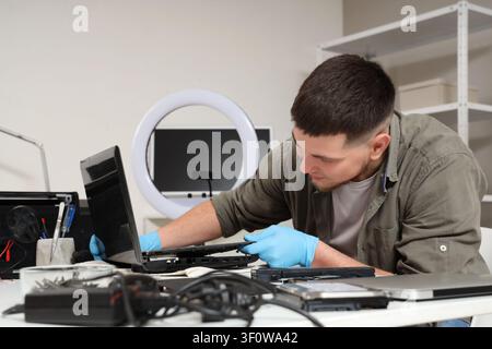 Male technician repairing laptop at table in service center Stock Photo