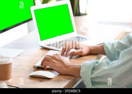 Person typing on a keyboard with a laptop and monitor green screens for digital content insertion Stock Photo