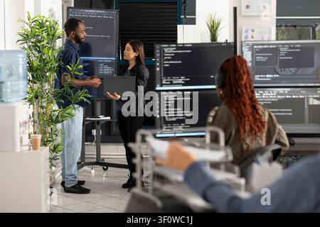 Professional team of software developers collaborates on code review in modern open office workspace. Programmers analyze data, discuss technical strategy and improve software performance together. Stock Photo