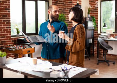 Business team brainstorms financial strategy around a laptop, analyzing reports and planning a management meeting for company growth in a startup office Stock Photo