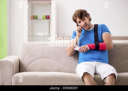 Young man with injured arm sitting on the sofa Stock Photo