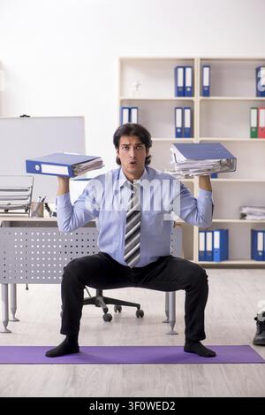 Young handsome male employee doing exercises in the office Stock Photo