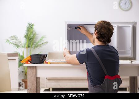 Young handsome contractor repairing fridge Stock Photo