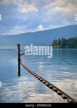 Moody evening view over Burrard Inlet from Barnet Marine Park in Burnaby, Metro Vancouver, with swimmers near the shoreline and mountains beyond. Stock Photo