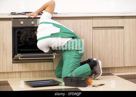 Young contractor repairing oven in kitchen Stock Photo