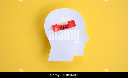 White Human Head Silhouette with Red Adhesive Tape and Handwritten Word Bias on Yellow Background Stock Photo