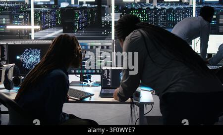 High tech server room collaborative team members work with visual programming workflow to detect equipment operational performance issues with engineering team team members check data analysis graph. Stock Photo