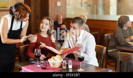 Young waitress taking order from young couple in restaurant Stock Photo