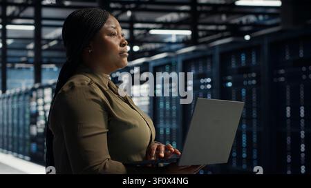 Software engineer in server facility working with notebook computer to update systems for increased stability. Stock Photo