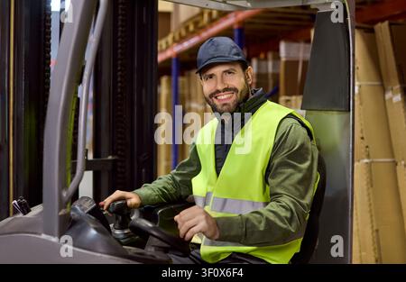 Smiling forklift driver operating in warehouse aisle with boxes and racks Stock Photo