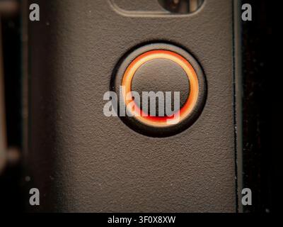 Macro extreme close-up of a circular black button illuminated by a glowing orange ring indicator on a textured device surface Stock Photo