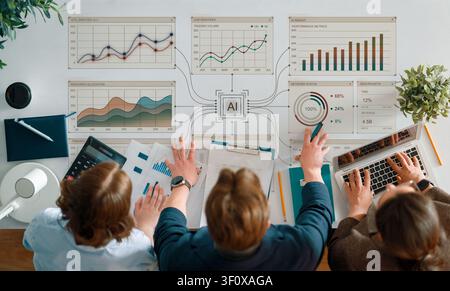 Top view of a diverse business team collaborating over data charts, digital reports, and AI-driven analytics on a modern office workspace. Charts, gra Stock Photo